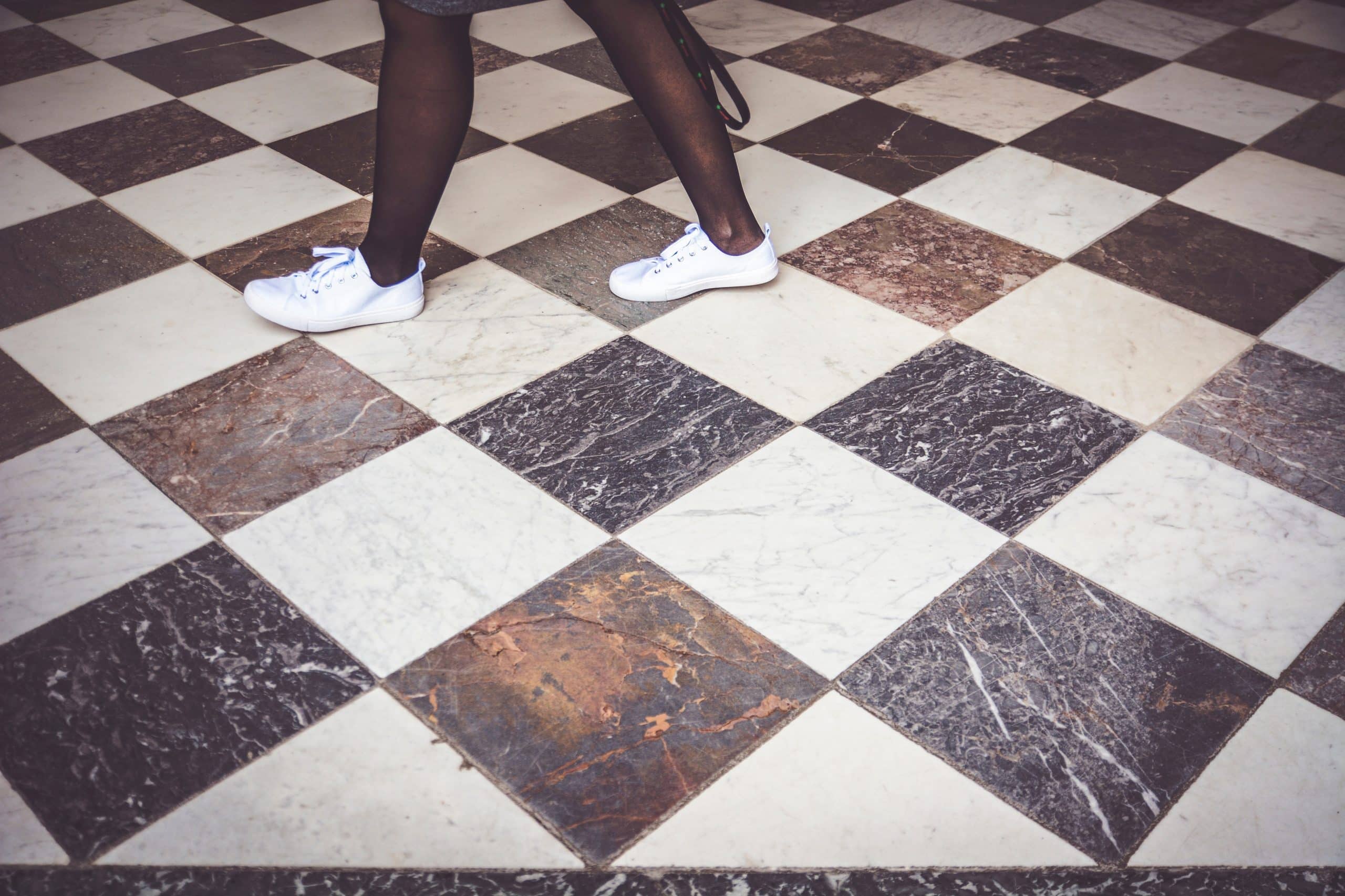 Jambes d'une jeune fille en train de marcher sur du carrelage noir et blanc