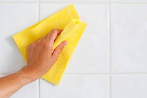 Main en train de nettoyer avec un chiffon jaune un sol carrelé