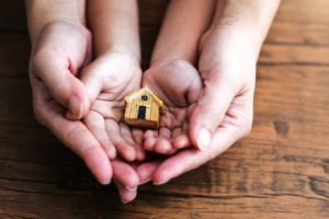 Parent tenant les mains de son enfant dans les siennes et une maison en bois en jouet