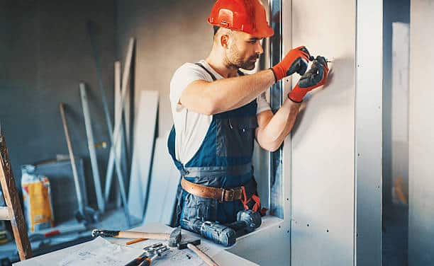 Homme qui visse une plaque de plâtre pour une cloison placo